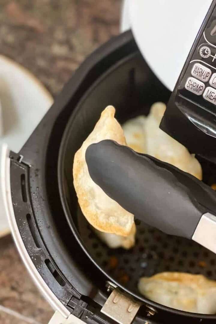 Frozen Pot Stickers in Air Fryer with tongs being pulled out