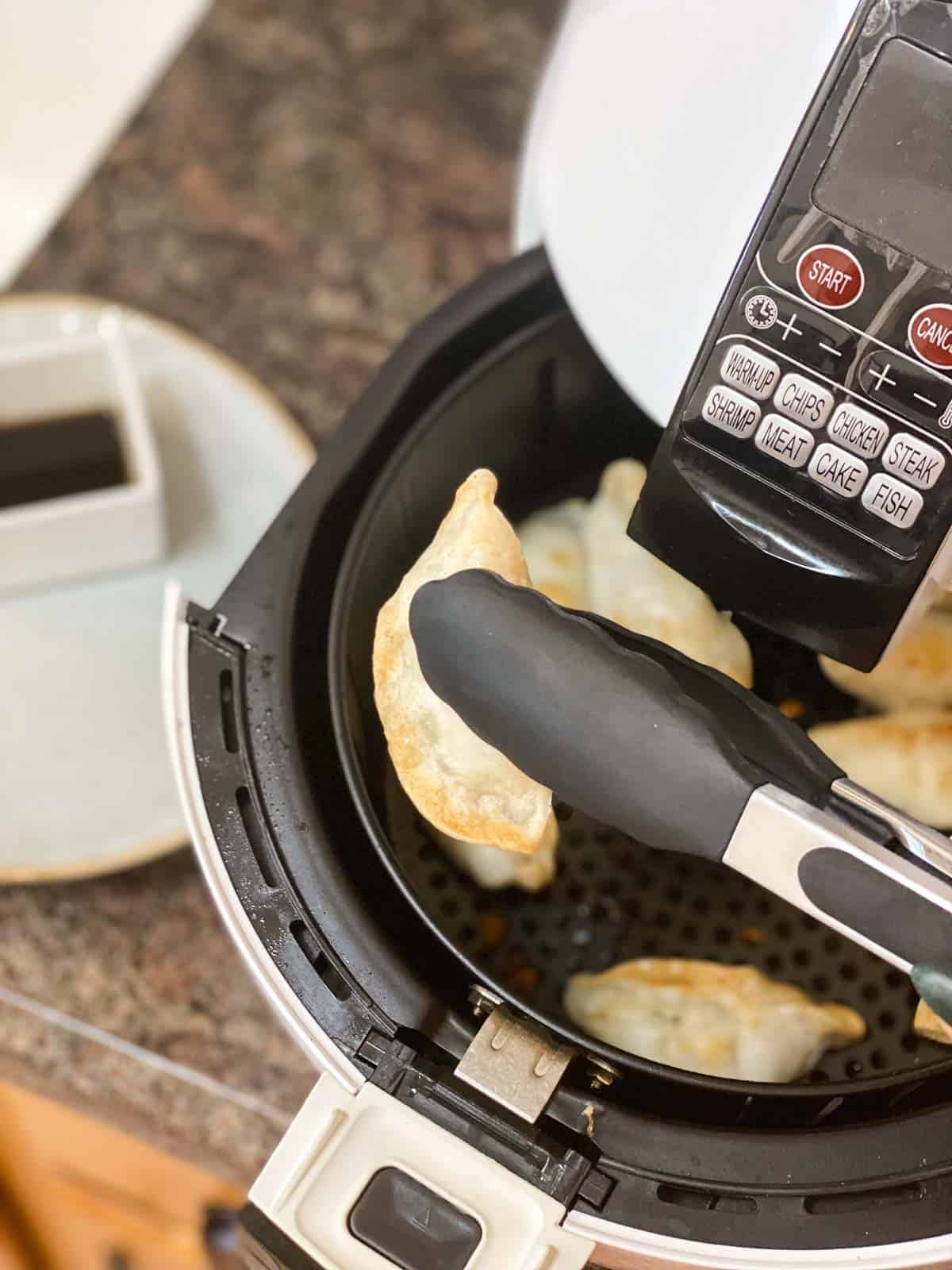 Tongs grabbing air fried potsticker out of air fryer.