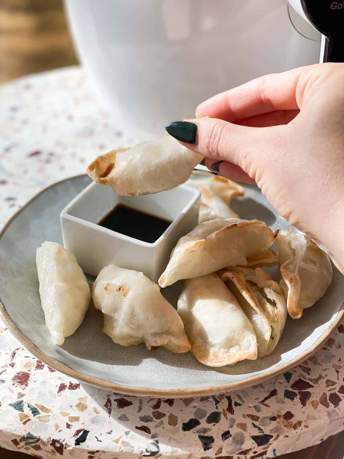 potsticker about to be dipped in soy sauce on a plate with other potstickers