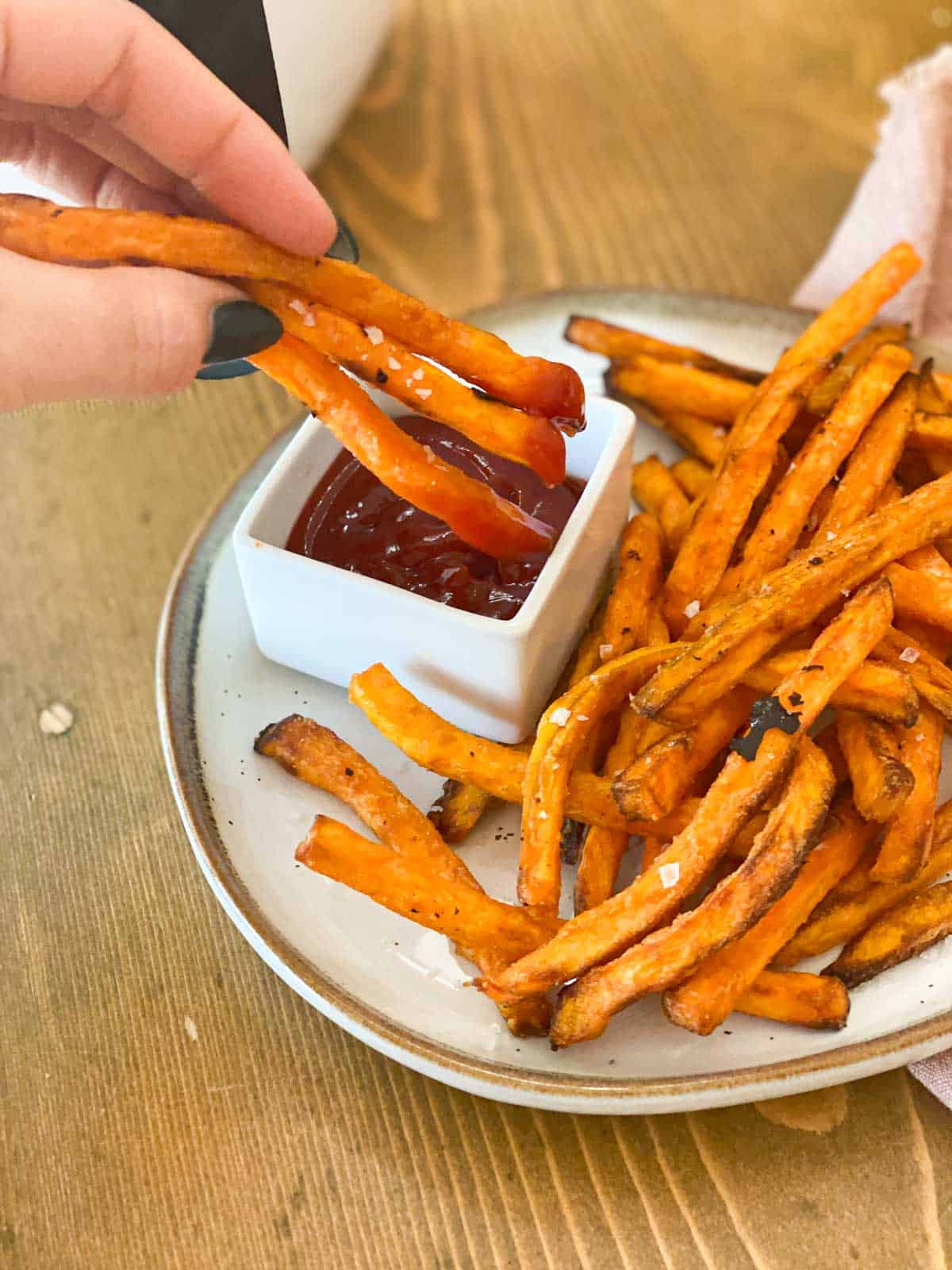 hand dipping sweet potato fries in ketchup