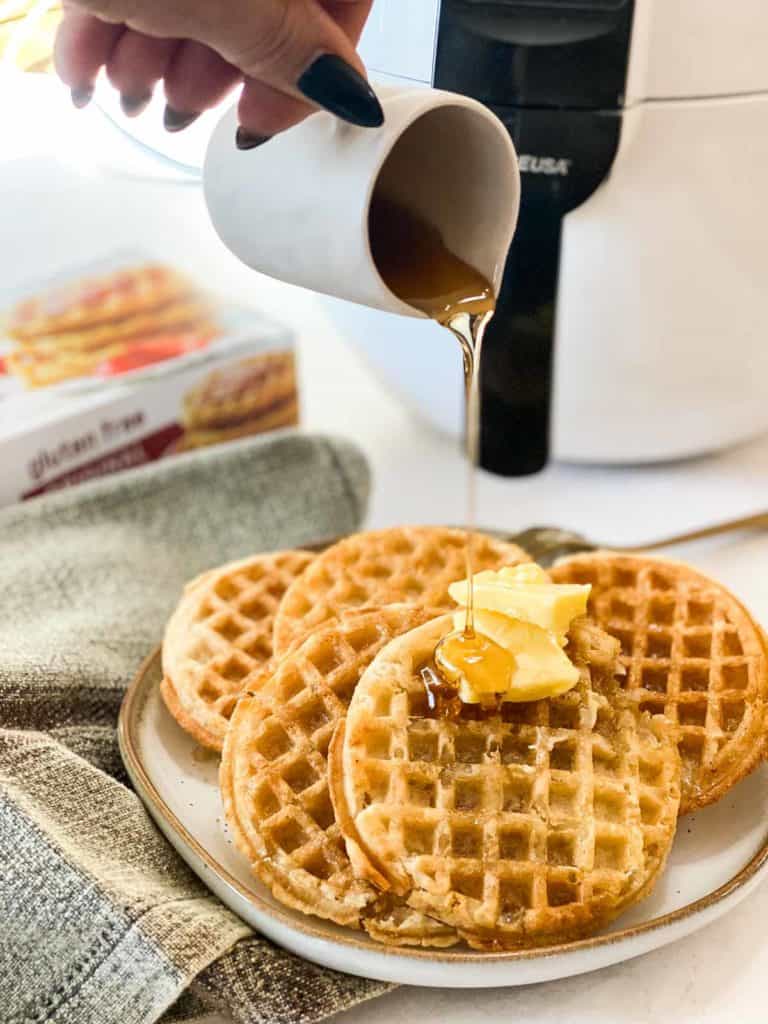 Frozen waffles on plate with butter and syrup being poured on top