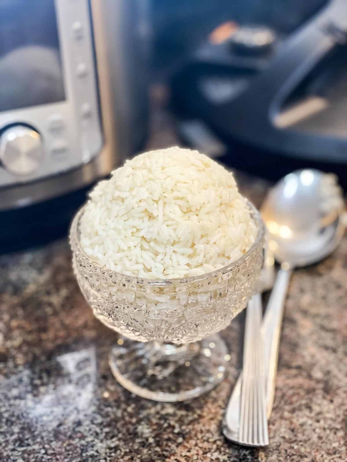 jasmine rice cooked and placed into a glass bowl with a spoon next to it and an instant pot in the background