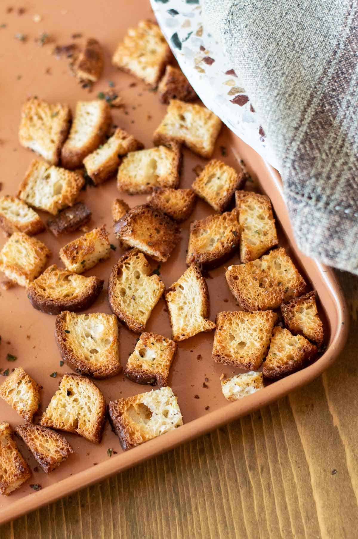 Cooked croutons spread on pink tray with seasoning on the tray.