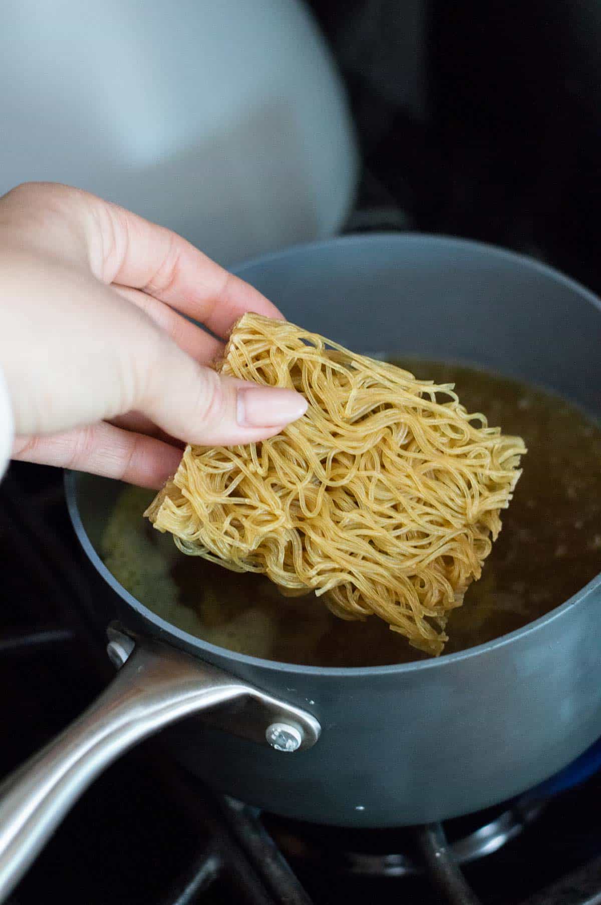 Gluten free ramen cake being dropped into pan of chicken stock 