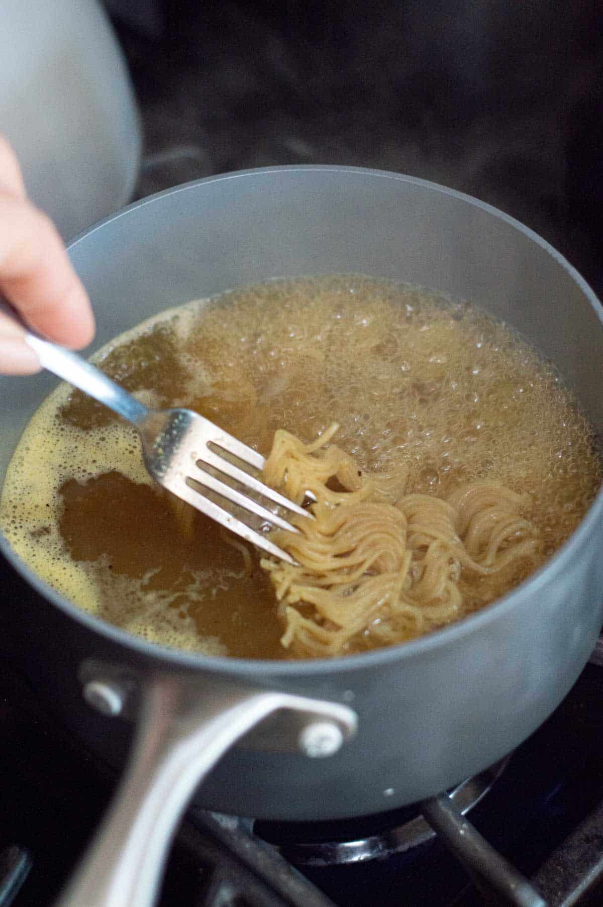gluten free ramen boiling in hot chicken stock being stirred by a silver fork 