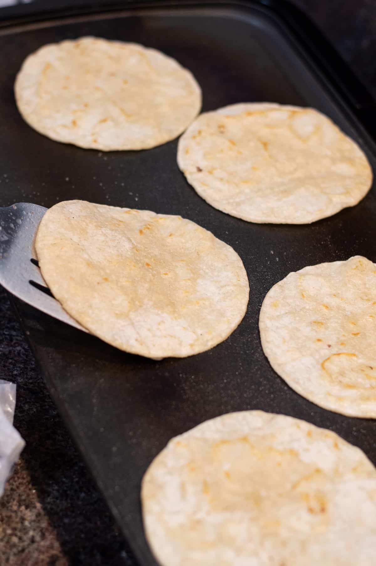 corn tortillas frying on the griddle