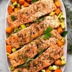 sheet pan salmon and veggies on a white plate with fresh herbs