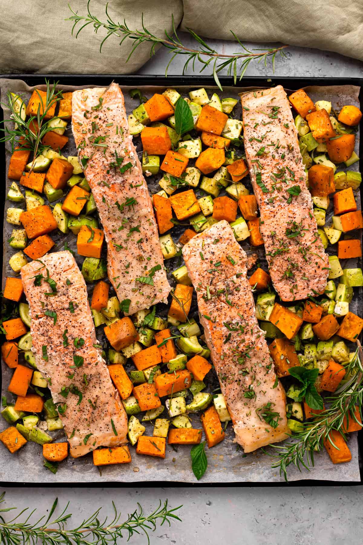 sheet pan salmon and veggies on a baking tray with herbs