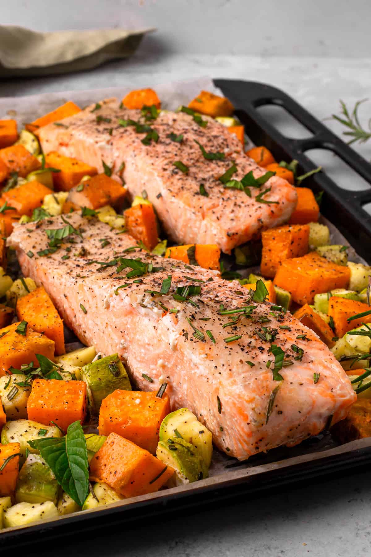 sheet pan salmon and veggies on a baking tray with fresh herbs after baking
