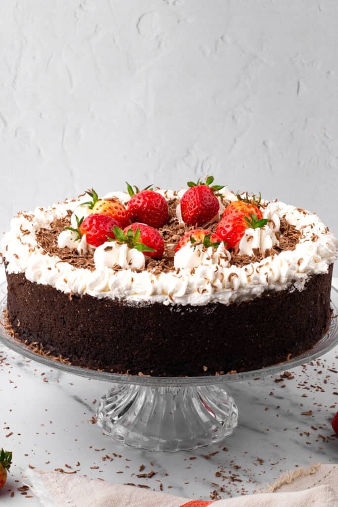 Side view of circle Gluten Free Banana Black Bottom Pie with a cookie crumb coating, whipped cream topping, and strawberries on top