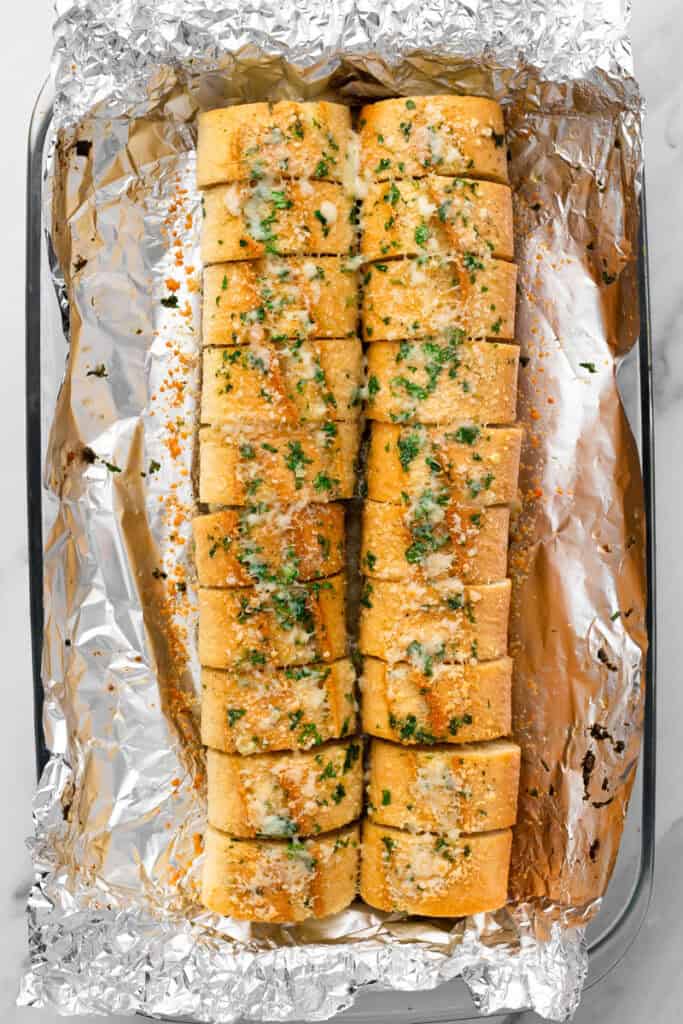gluten free garlic bread sliced on tinfoil with butter and parsley and parmesan