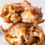 Two fluffy fried gluten free apple fritters with a glaze stacked on top of each other with the inside texture showing.