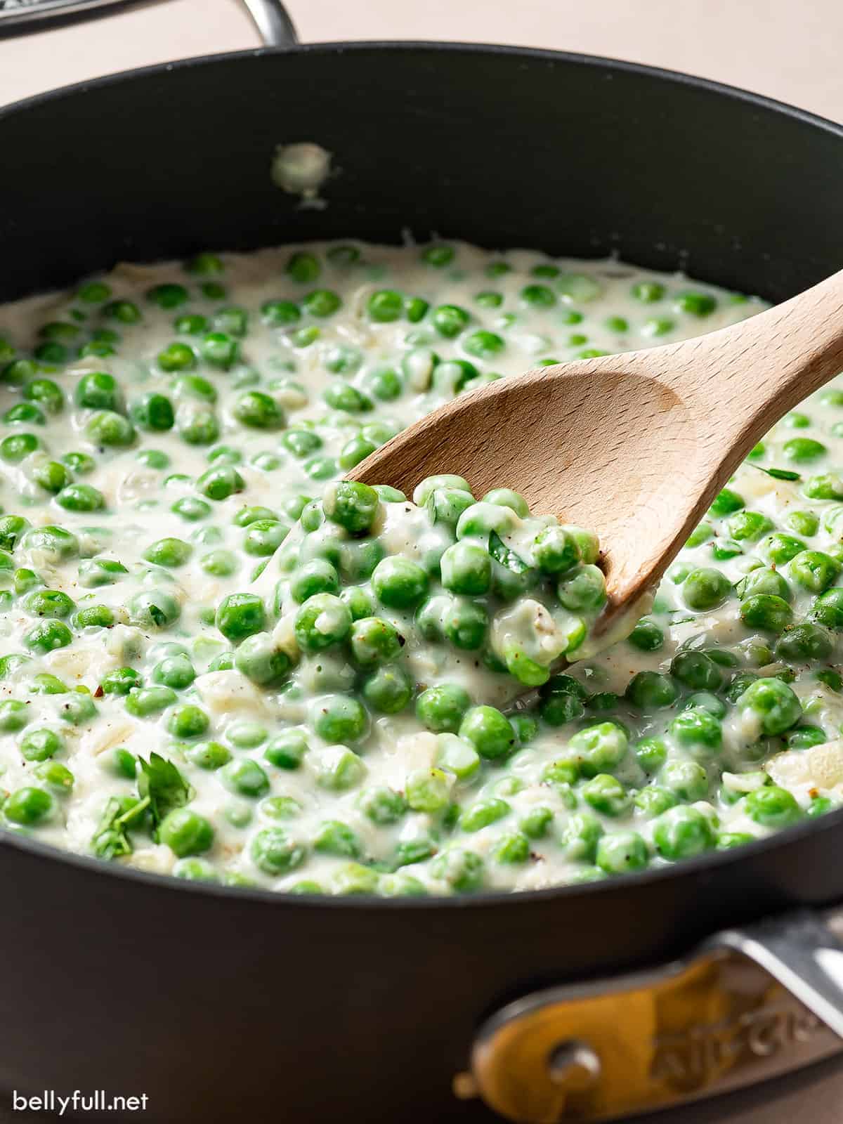 Homemade creamed peas in a pan. A wooden spoon is stirring the peas 