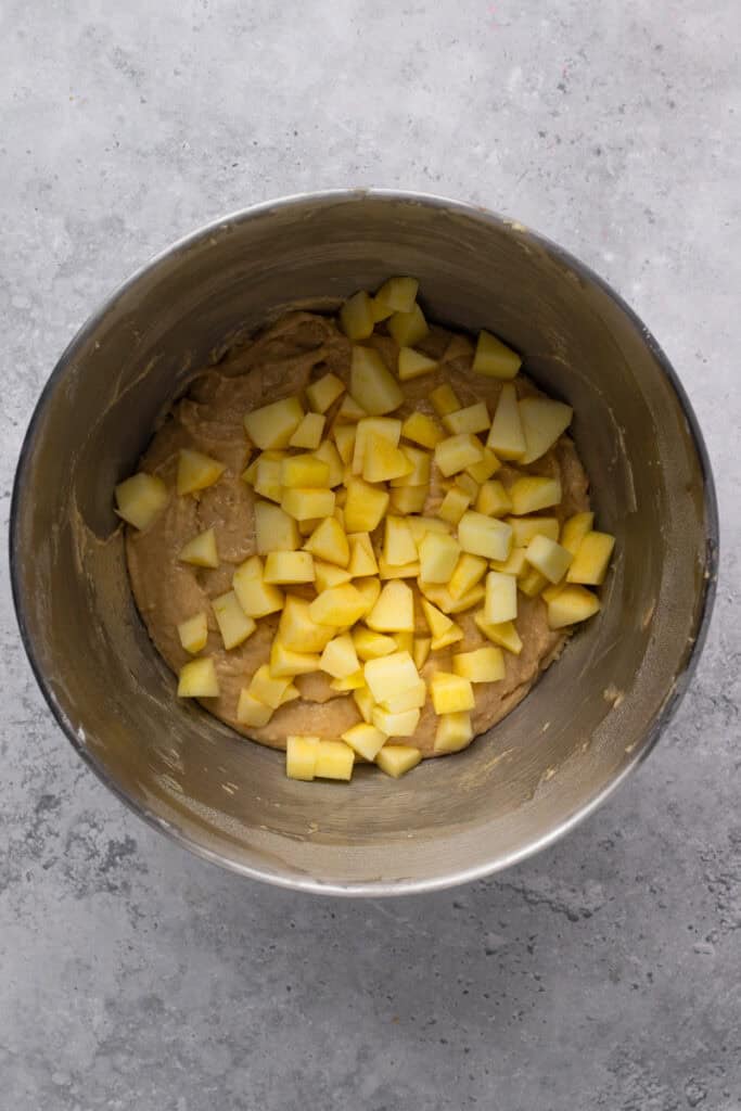 Gluten free apple fritter ingredients in a bowl with apples on top ready to be folded in.