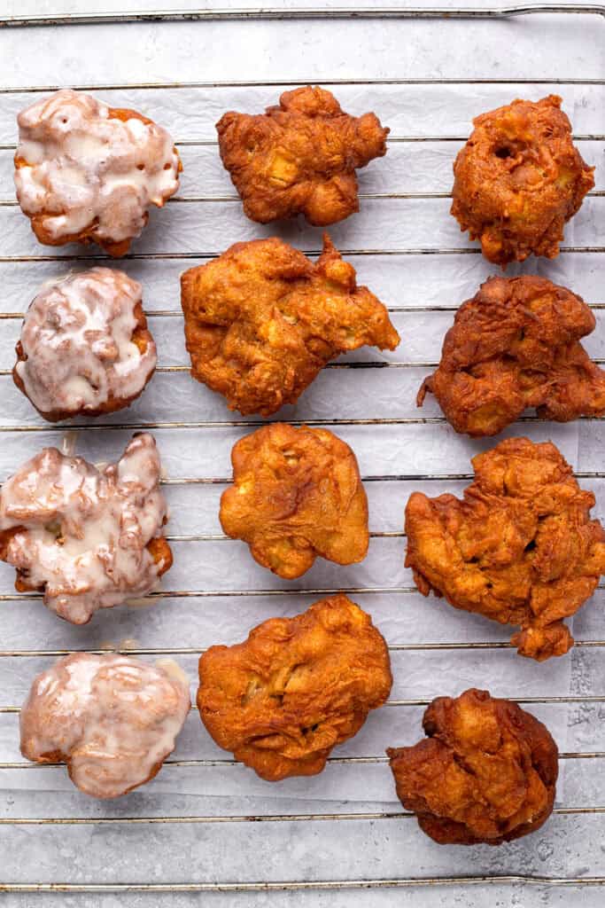Fluffy fried gluten free apple fritters with a glaze on a wire rack.