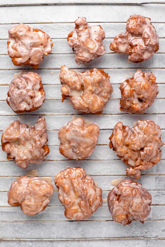 Fluffy fried gluten free apple fritters with a glaze on a wire rack.