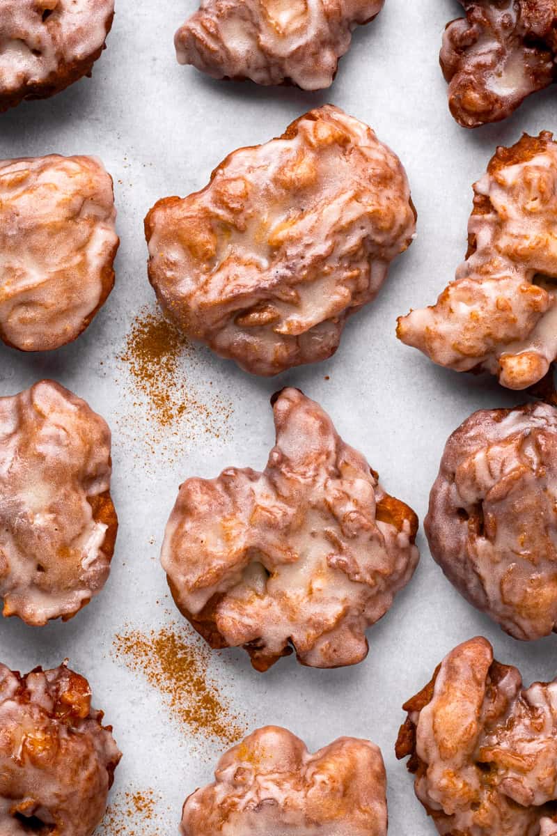Fluffy fried gluten free apple fritters with a glaze on a marble board.