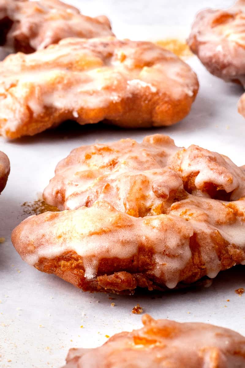 Fluffy fried gluten free apple fritters with a glaze on a marble board.