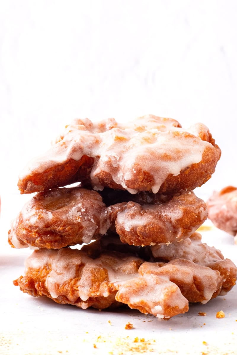 Three fluffy fried gluten free apple fritters with a glaze on a marble board.