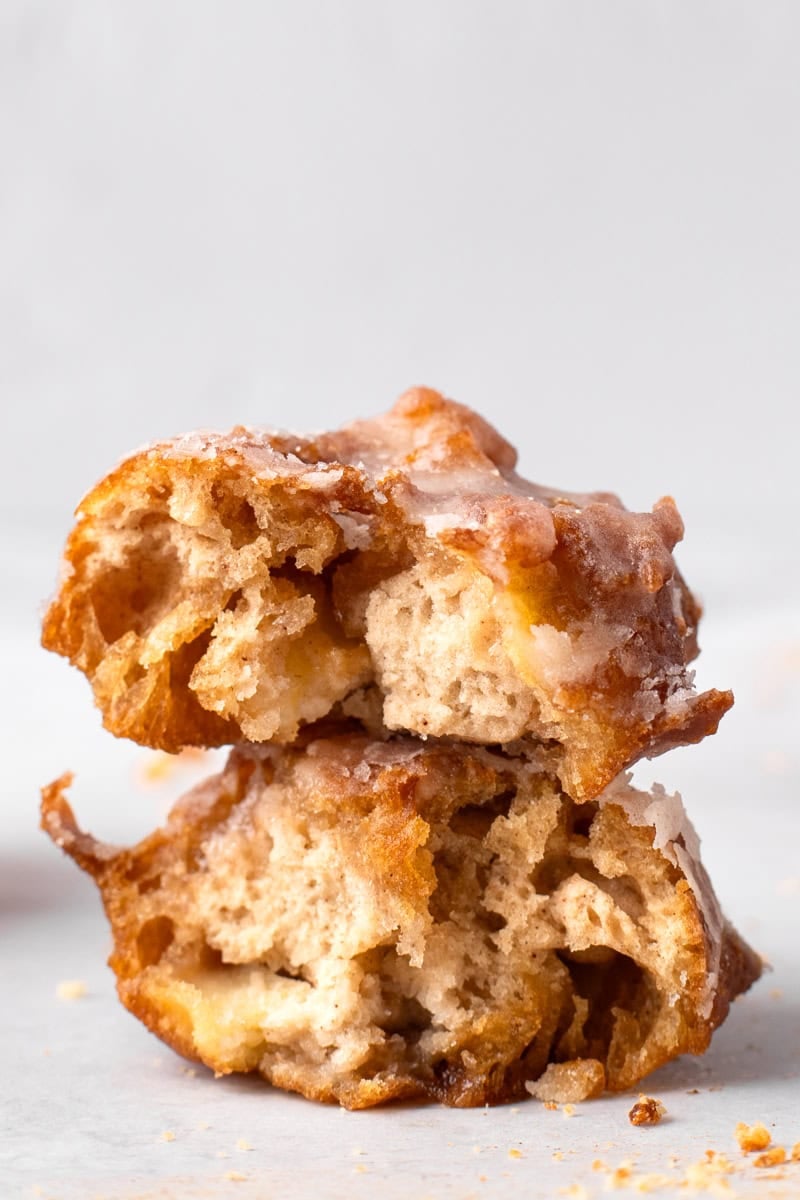 Two fluffy fried gluten free apple fritters with a glaze stacked on top of each other with the inside texture showing.