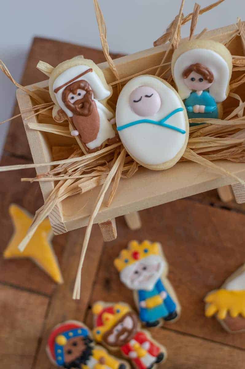 Nativity cookies in a manger. Joseph, Jesus, and Mary are in the manger will straw. The star and wise men cookies are in the background.