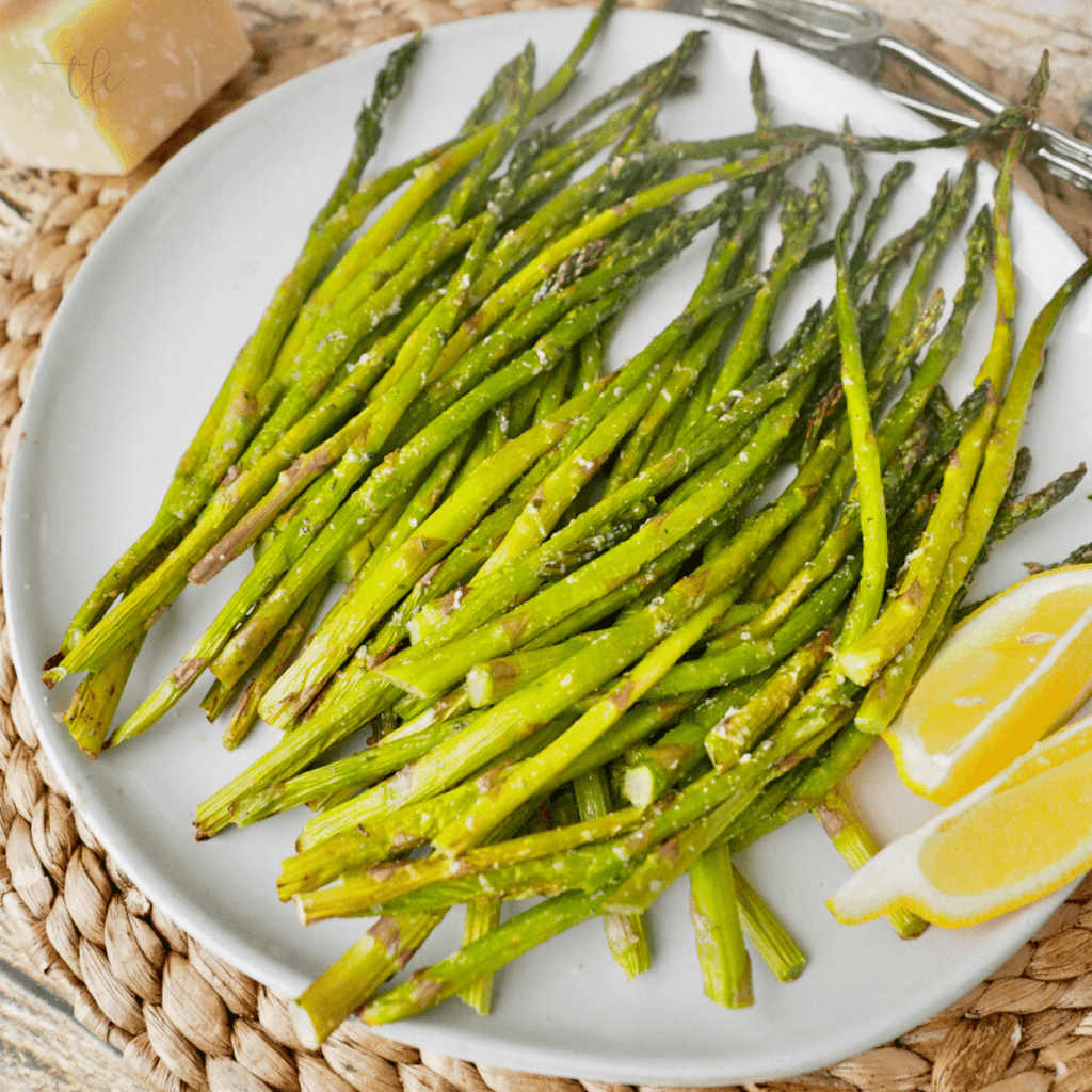 Air fryer asparagus on a white plate with two lemon slices next to them