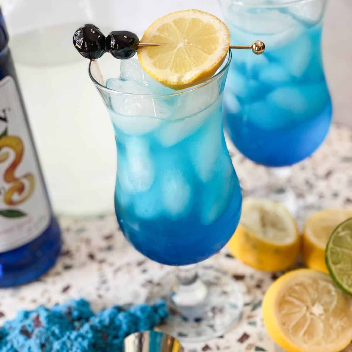 Blue lagoon mocktail with a lemon on a stirrer on top of the glass