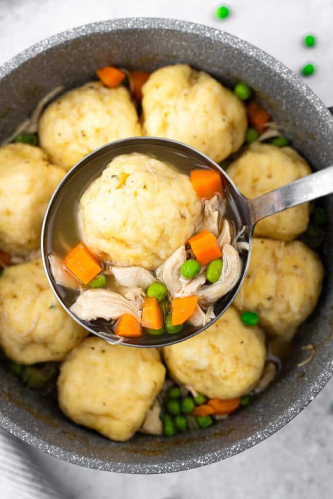 spoon full of chicken and dumplings with pot of chicken and dumplings in the back