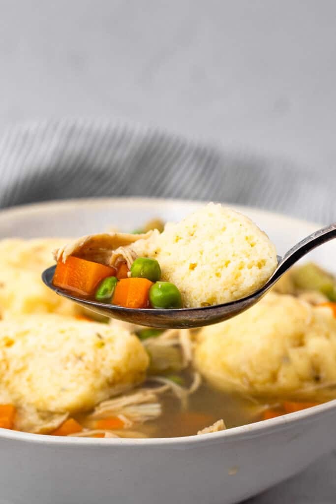 square image of spoon full or chicken and dumplings with bowl of gluten free chicken and dumplings in the back