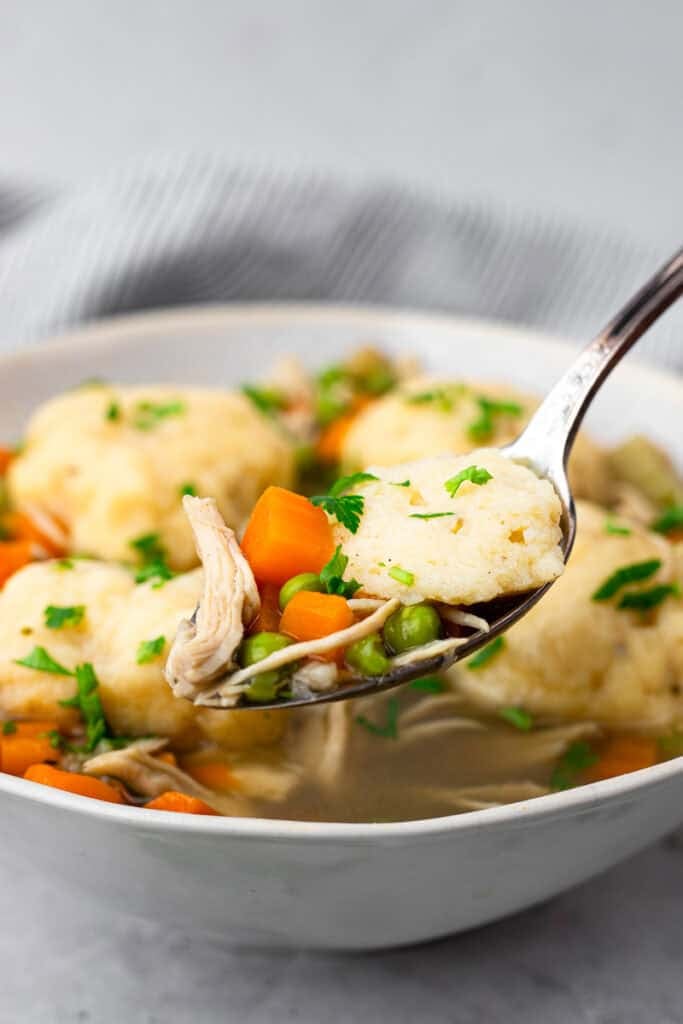 square image of spoon full or chicken and dumplings with bowl of gluten free chicken and dumplings in the back