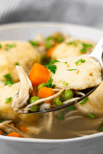 square image of spoon full or chicken and dumplings with bowl of gluten free chicken and dumplings in the back