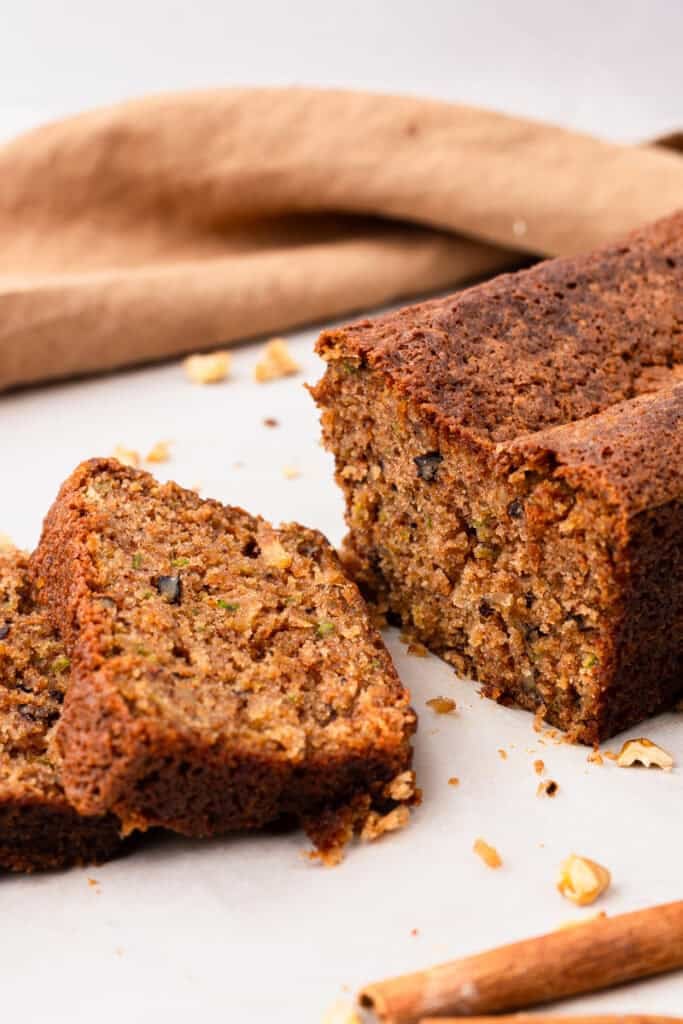 side view of Extra Moist Gluten Free Zucchini Bread on a plate with two slices cut out of the bread with crumbs on the plate