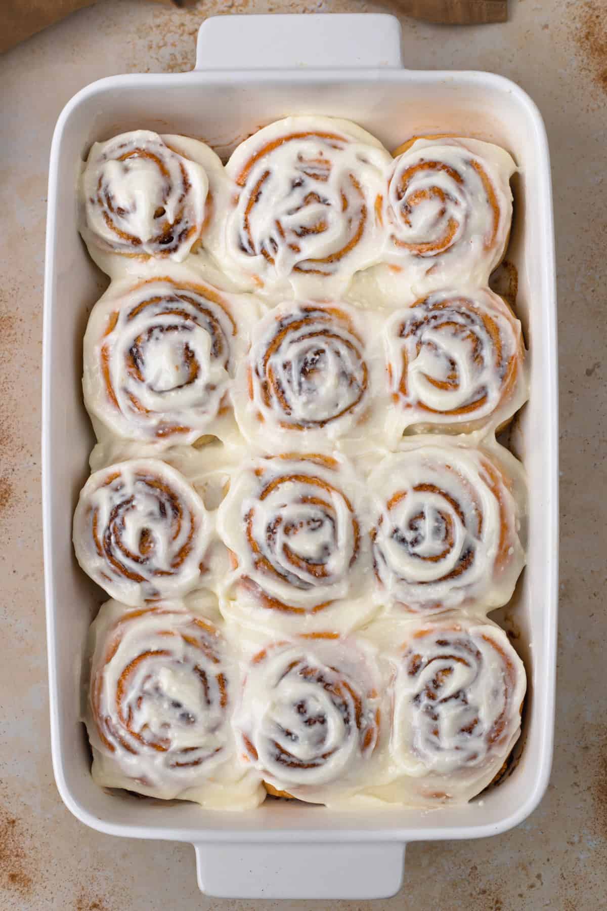 Close-up of frosted gluten-free cinnamon rolls in a white baking dish.