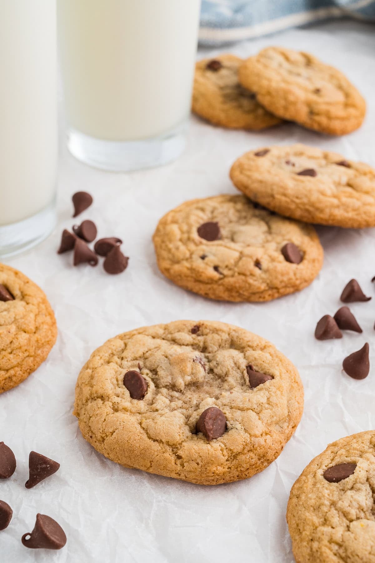 Gluten free chocolate chip cookies on a plate with chocolate chips off the plate by the side and milk in the background.