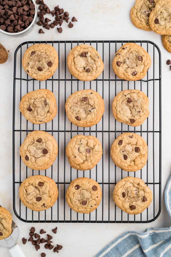 Gluten free chocolate chip cookies on a wire rack with chocolate chips off to the side.