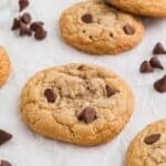 Gluten free chocolate chip cookies on a plate with chocolate chips off the plate by the side and milk in the background.