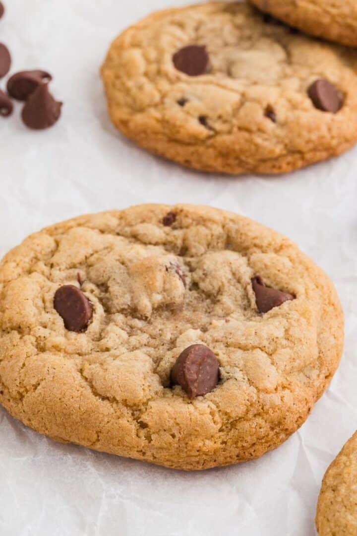 Gluten free chocolate chip cookies on a plate with chocolate chips off the plate by the side and milk in the background.