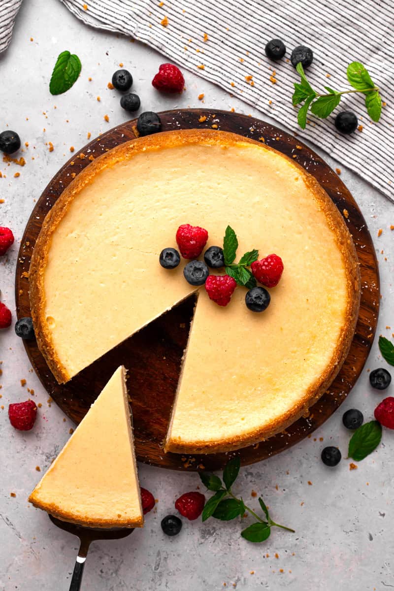 New York Style Gluten Free Cheesecake with berries and mint on top and a slice coming out