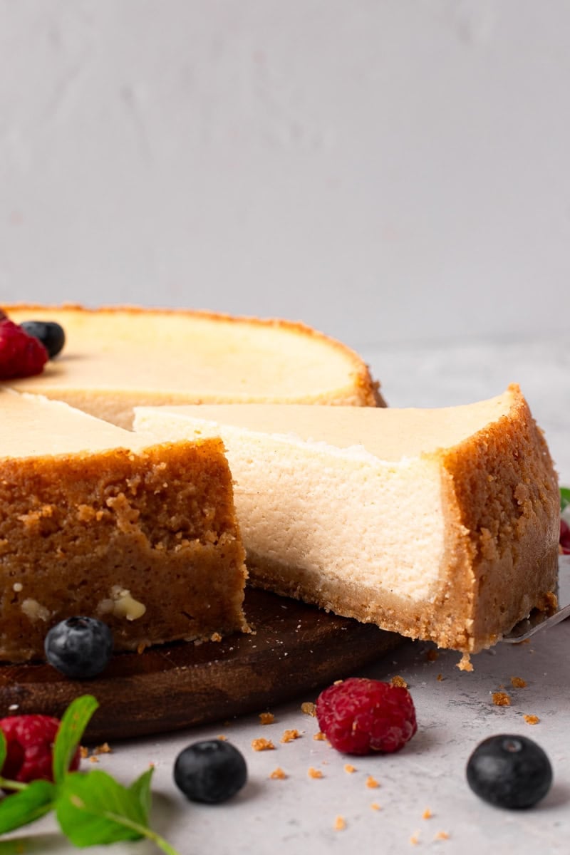 New York Style Gluten Free Cheesecake with berries and mint on top and a slice coming out