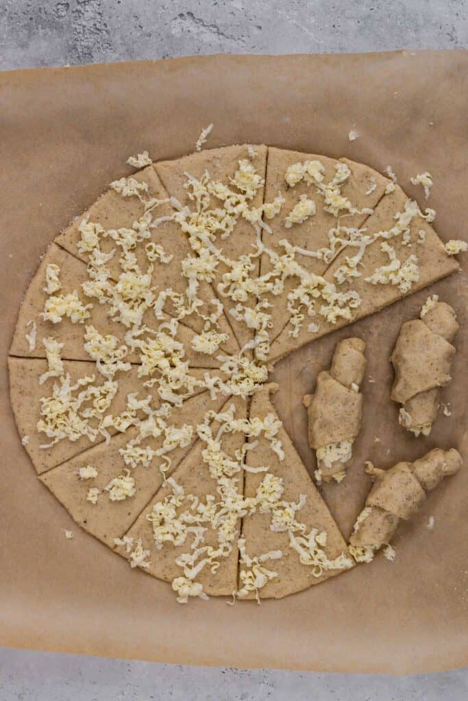 gluten free crescent roll dough rolled out into a circle with triangles cut and butter grated on top with a few rolled into crescent rolls