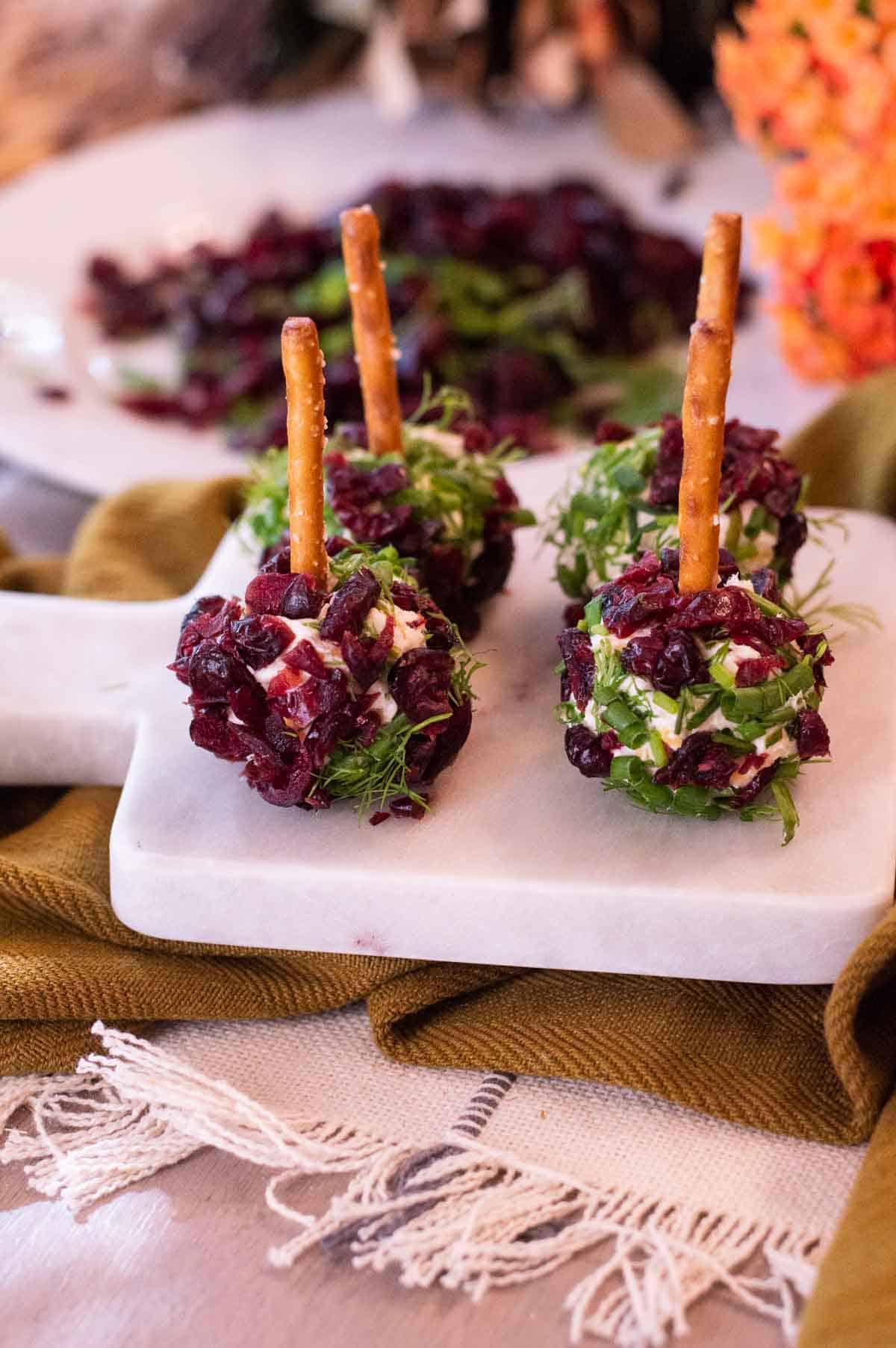 Mini Cheeseballs with Pretzel Toothpicks and cranberries and fresh herbs on a marble tray