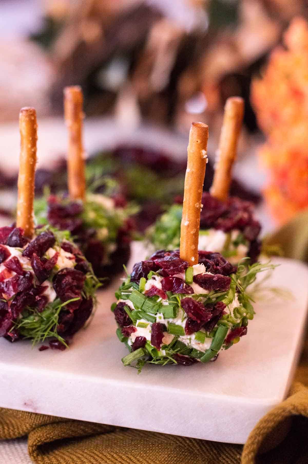 Mini Cheeseballs with Pretzel Toothpicks and cranberries and fresh herbs on a marble tray