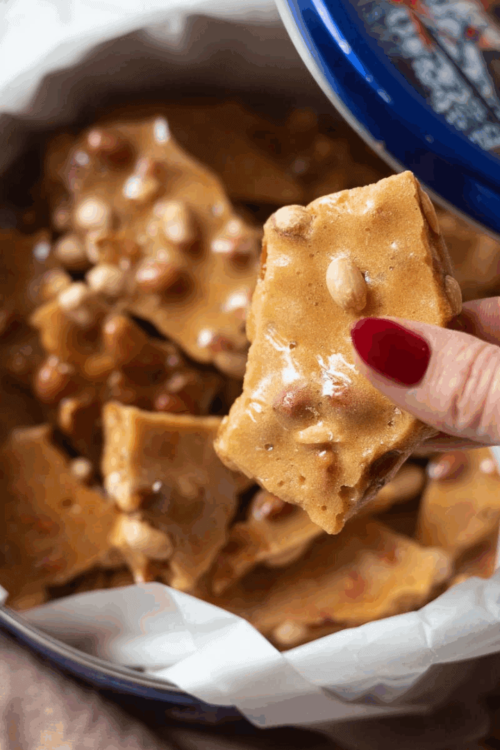 top down image of hand holding gluten free peanut brittle pieces in a tin