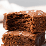 two gluten free brownies stacked on top of each other on a plate to show texture, one brownie with a bite taken out of it