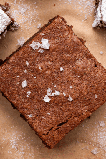 Chewy and decadent gluten free brownie on brown parchment paper with flakey sea salt on top