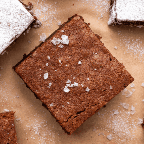 Chewy and decadent gluten free brownie on brown parchment paper with flakey sea salt on top