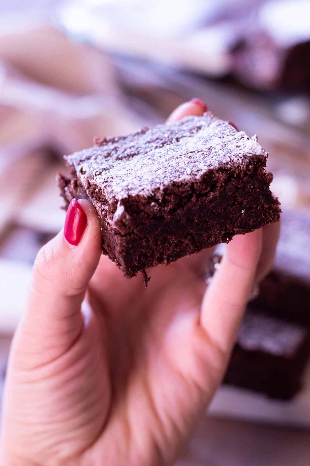 chewy gluten free brownies with powdered sugar and a hand holding it