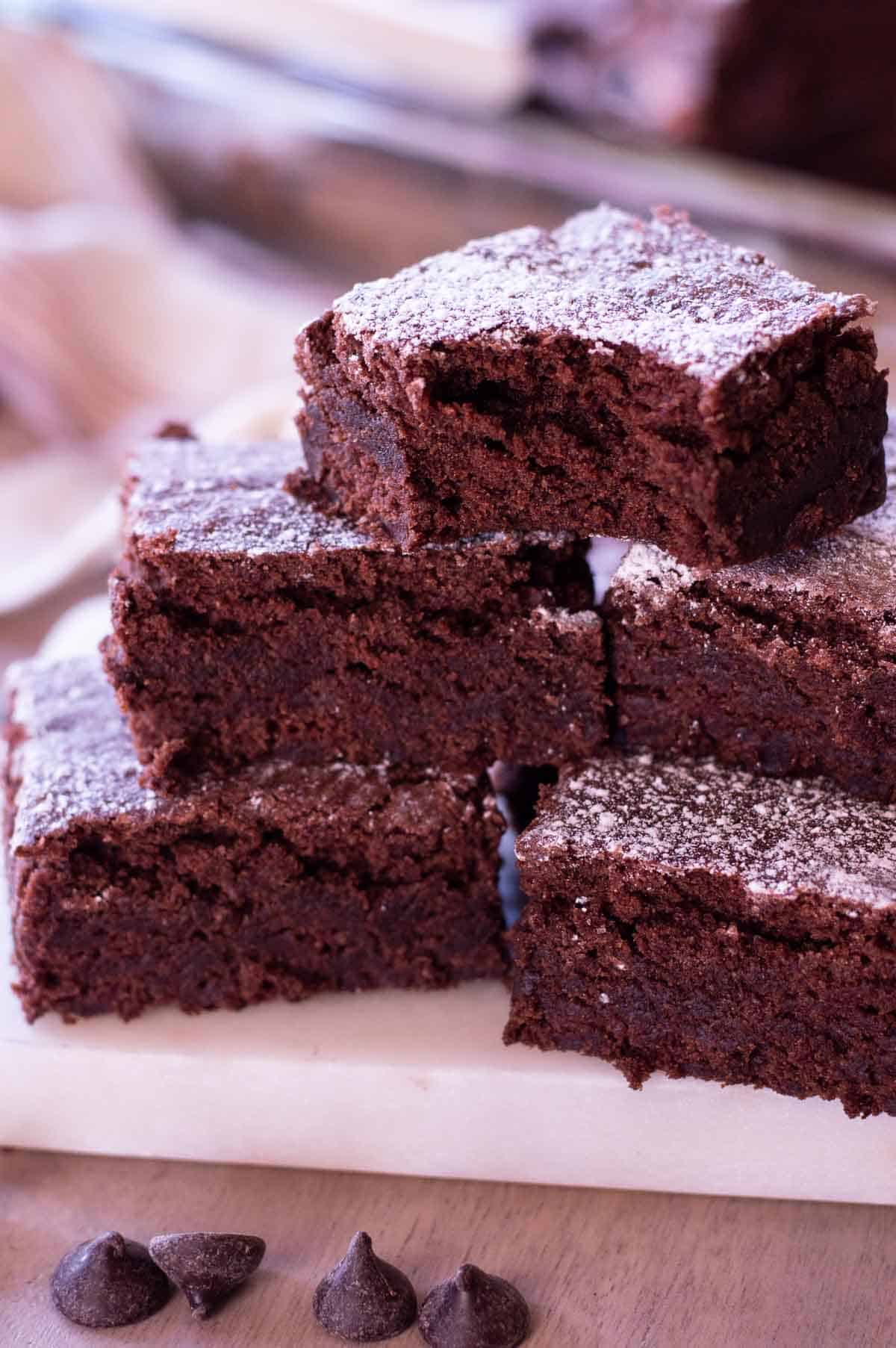 chewy gluten free brownies stacked on each other with powdered sugar and a bite taken out of one
