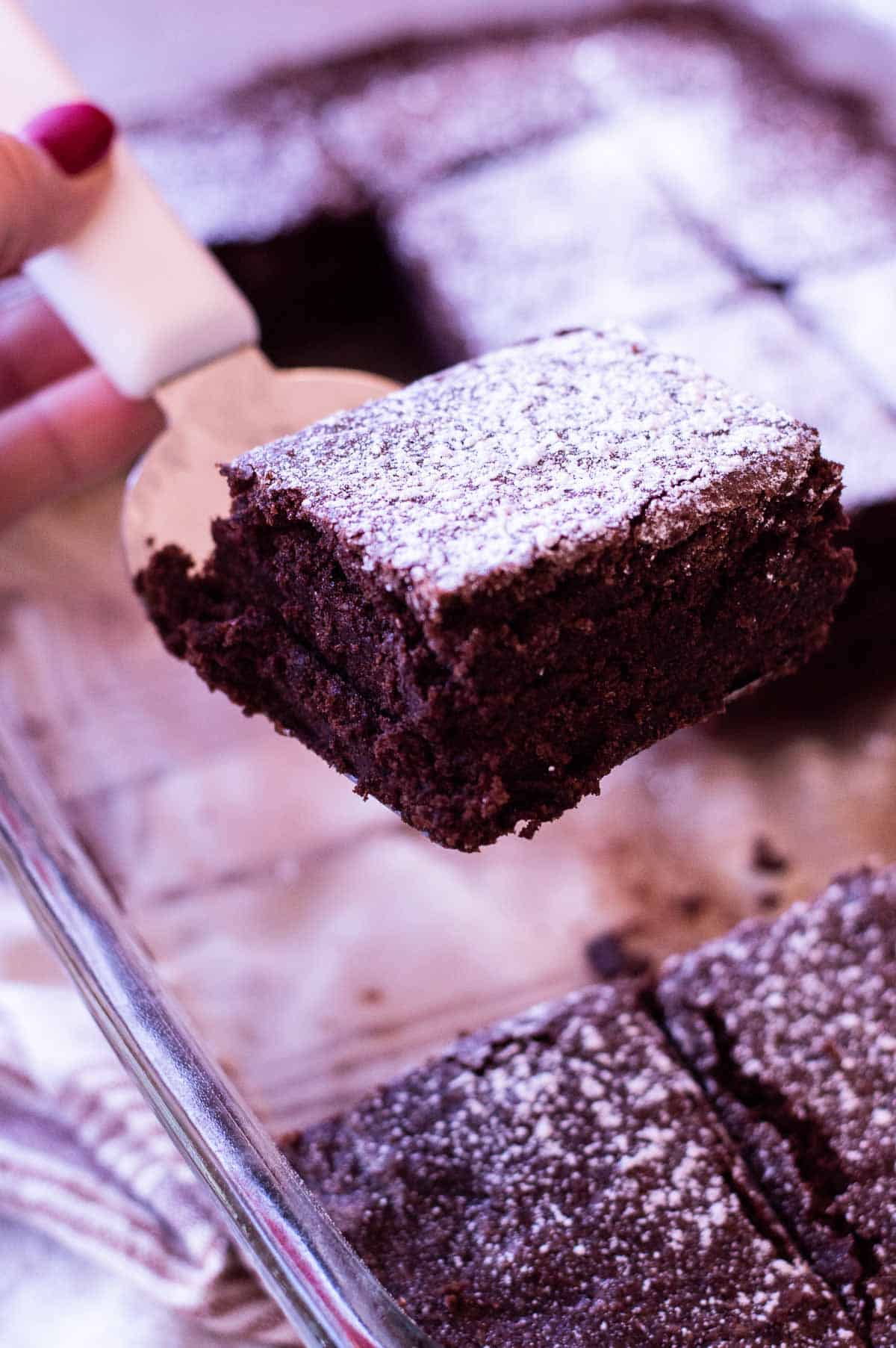 chewy gluten free brownies on a spatula being lifted out of a pan