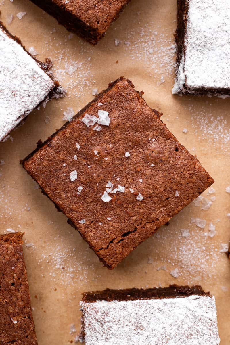 gluten free brownie with flakey sea salt on top sitting on brown parchment paper